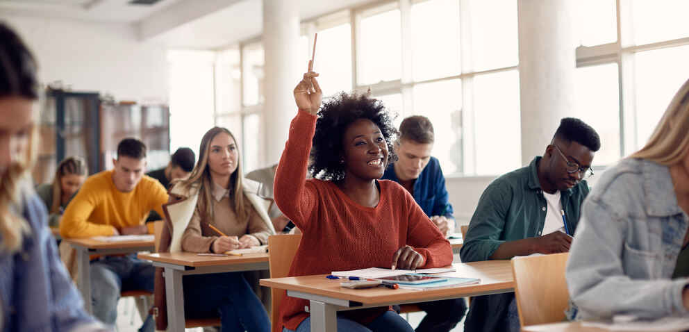 Happy black student raising arm to answer question while attending class with her university colleagues.